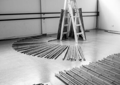 b&w photo of a dance studio filled with bamboo ready for an art installation. Their is bamboo on the floor and some leaned against a ladder