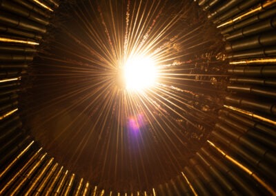 a photo taken at night inside a round bamboo art installation structure with gold leaf applied with some of the bamboo poles and a warm light above, causing a magenta lens flare