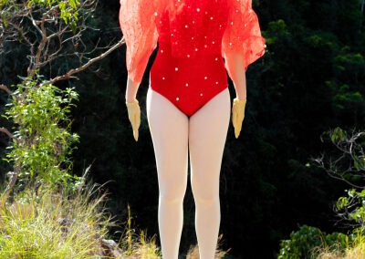 self portrait of a women with bright red hair wearing a red leotard and red tulle collar with white tight, jumping, suspended in mid air. The shot was taken in nature.