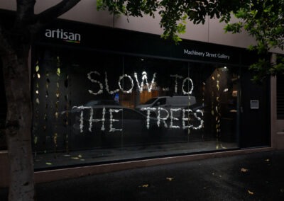 photo of a window art gallery. The window shows white lettering (spelt out in porcelain letters) 'SLOW TO THE TREES'.