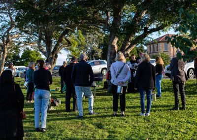 folks in a park listening to an artist under a tree reading from a4 paper print outs