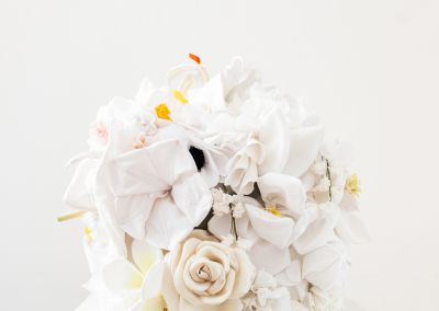 white handmade fabric flowers, appear on top of a plinth within a white walled gallery. The flowers are constructed into a cube.
