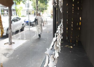 a shot inside a window gallery in a city, it looks out to cars and trees and pedestrian walking by