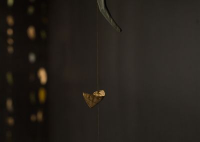 close up shot of a window gallery installation it shows fabric gold leaves hanging against a charcoal painted background